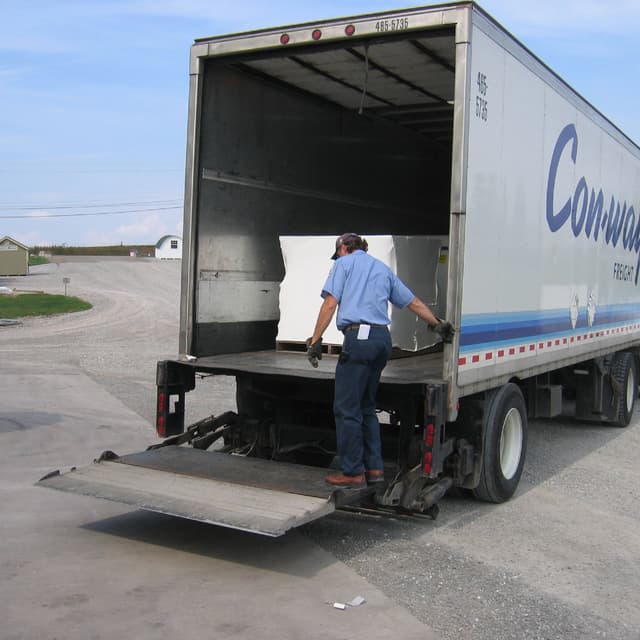 Packaged playhouse kit in white shrink wrap being loaded onto semi truck trailer.