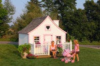 8x8 Gingerbread Cottage Playhouse with deck and rail. A girl is rolling a stroller in front 